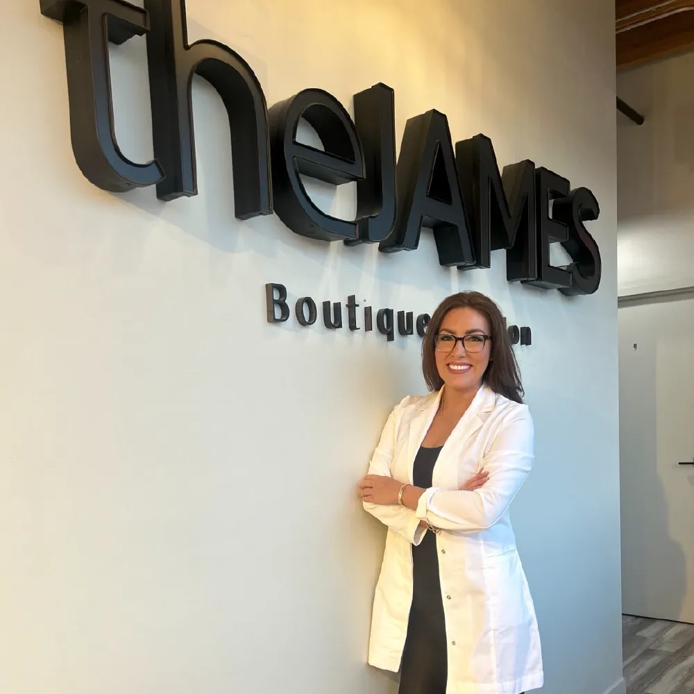 Dr. Jess, Chiropractic Specialist, standing in front of a wall sign reading The James Boutique in Ada Michigan.