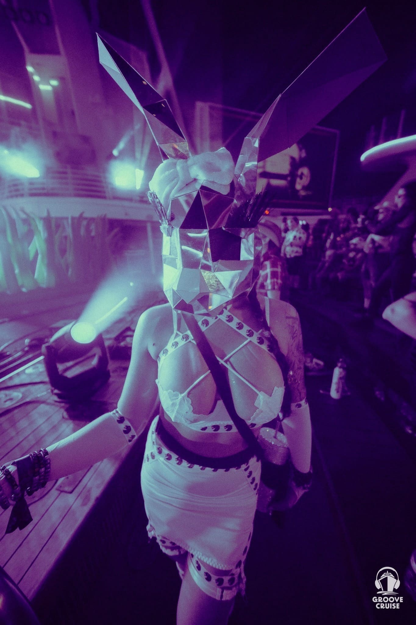 Woman dressed in festival outfit wearing a mirrored rabbit mask on Groove Cruise ship deck at night