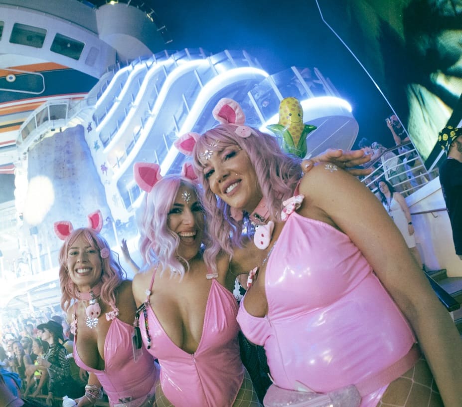 Group of women wearing pink festival costumes enjoying a late-night set under full production lighting on rave cruise