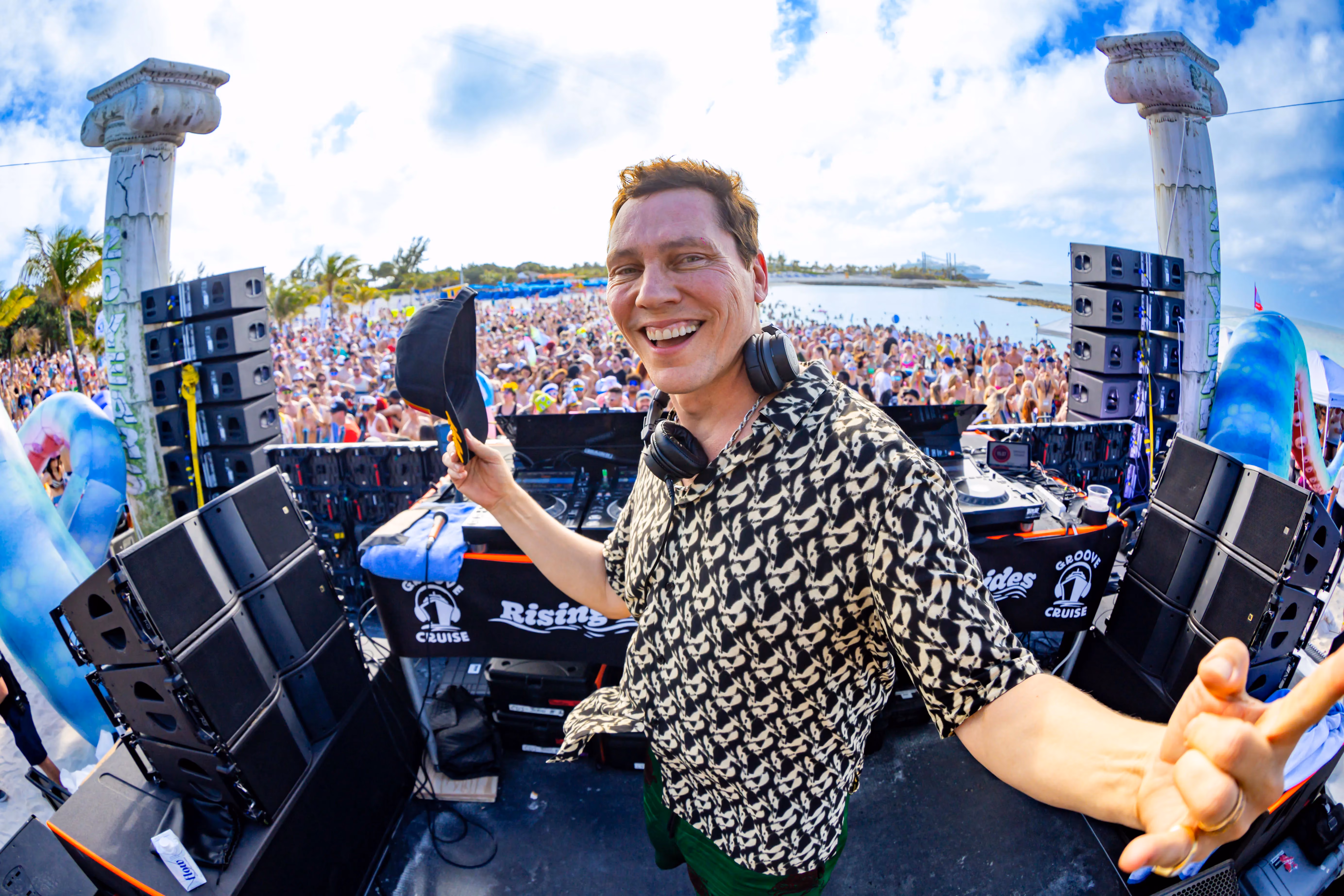 Tiesto performing on stage with fans cheering at Groove Cruise island party