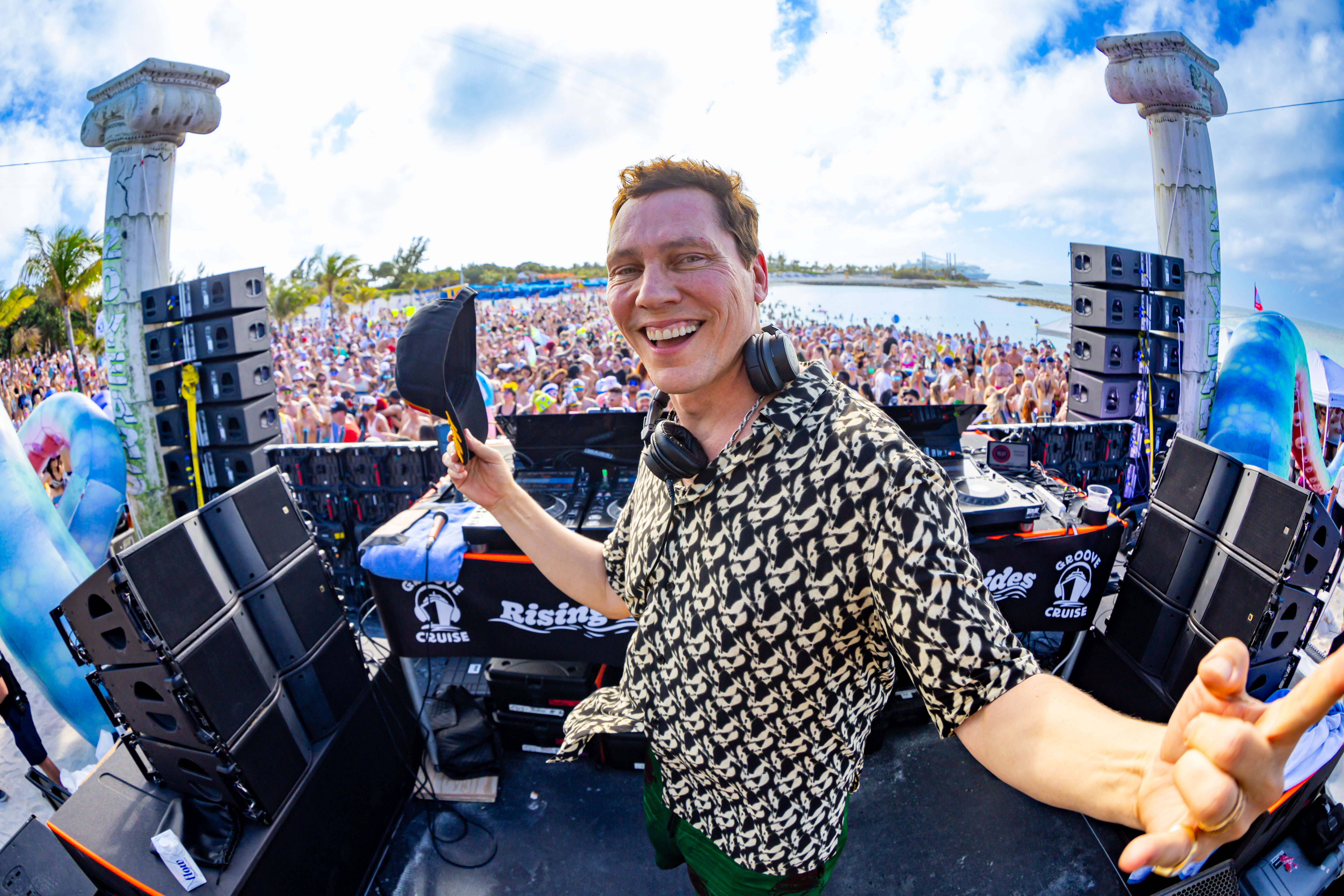 Tiesto performing on stage with fans cheering at Groove Cruise island party