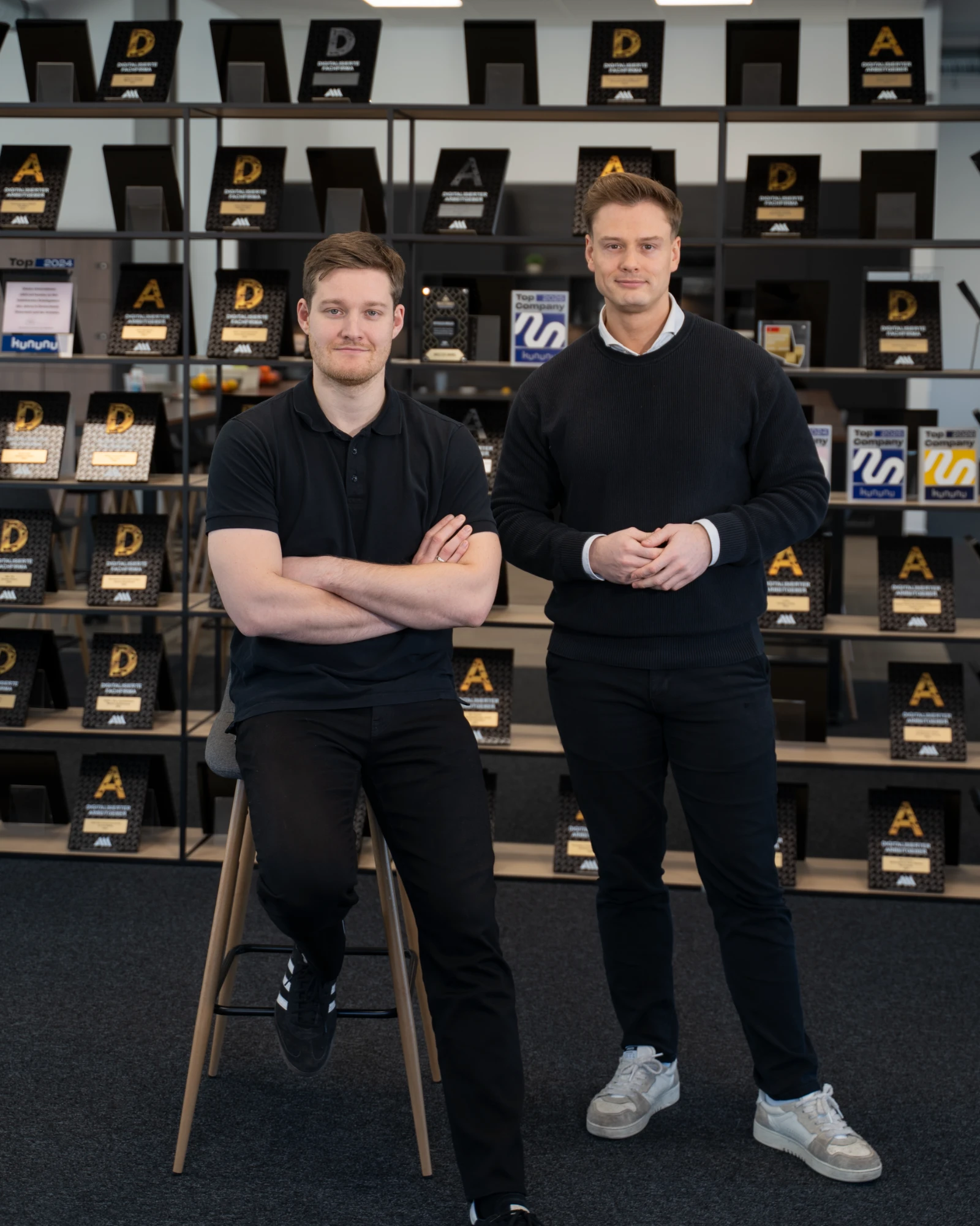 Marvin Flenche und Alexander Thieme vor der Award-Wand der A&M Unternehmerberatung