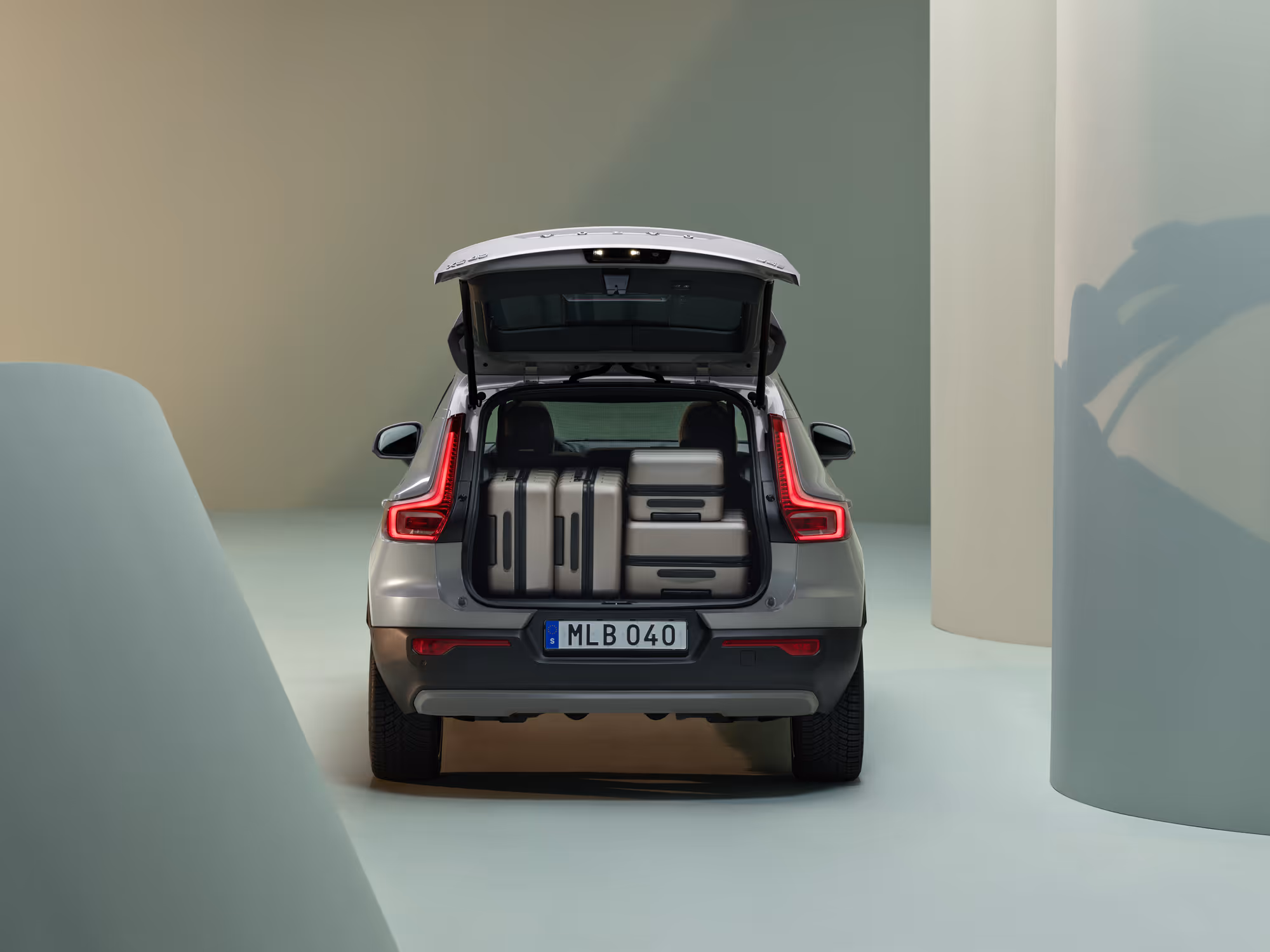 Rear view of a silver SUV with open trunk containing four beige suitcases in a minimalist studio setting.