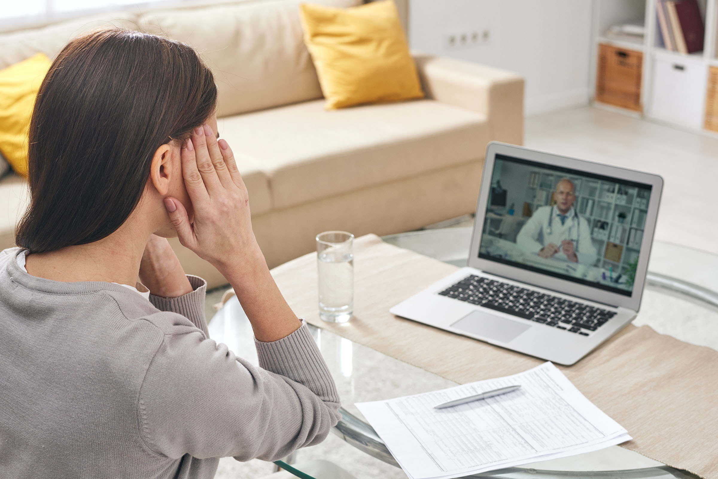 Remote Dental Consultation A woman sits at home, holding her jaw in discomfort while having a video consultation with a healthcare professional on her laptop