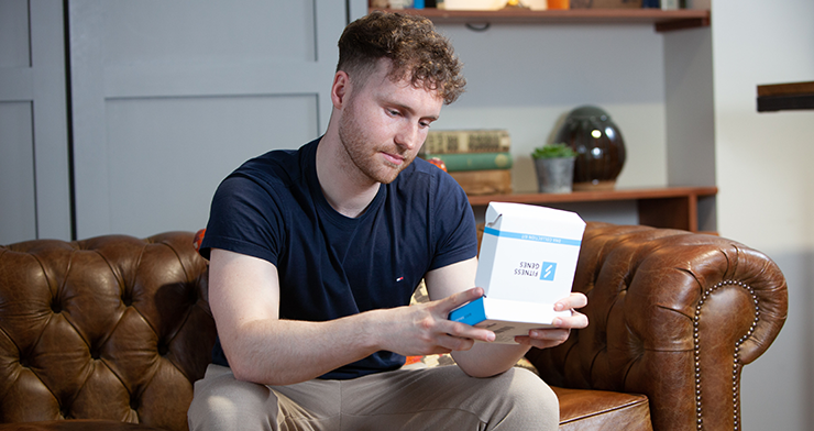 A man sat on a sofa holding a FitnessGenes DNA testing kit