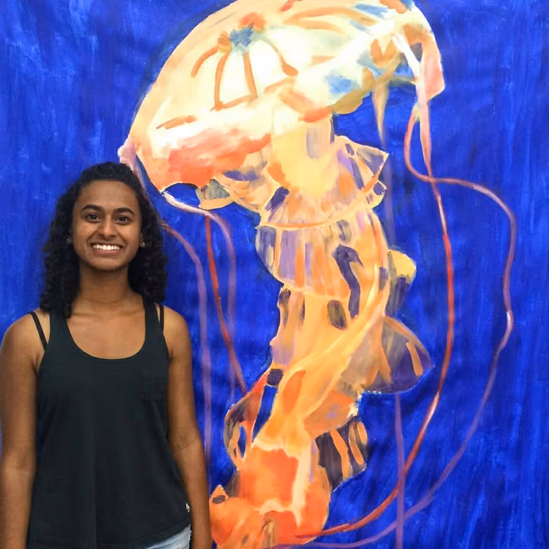 Veena B., Portfolio Program graduate, happily standing next to her large-scale painting of a jellyfish.