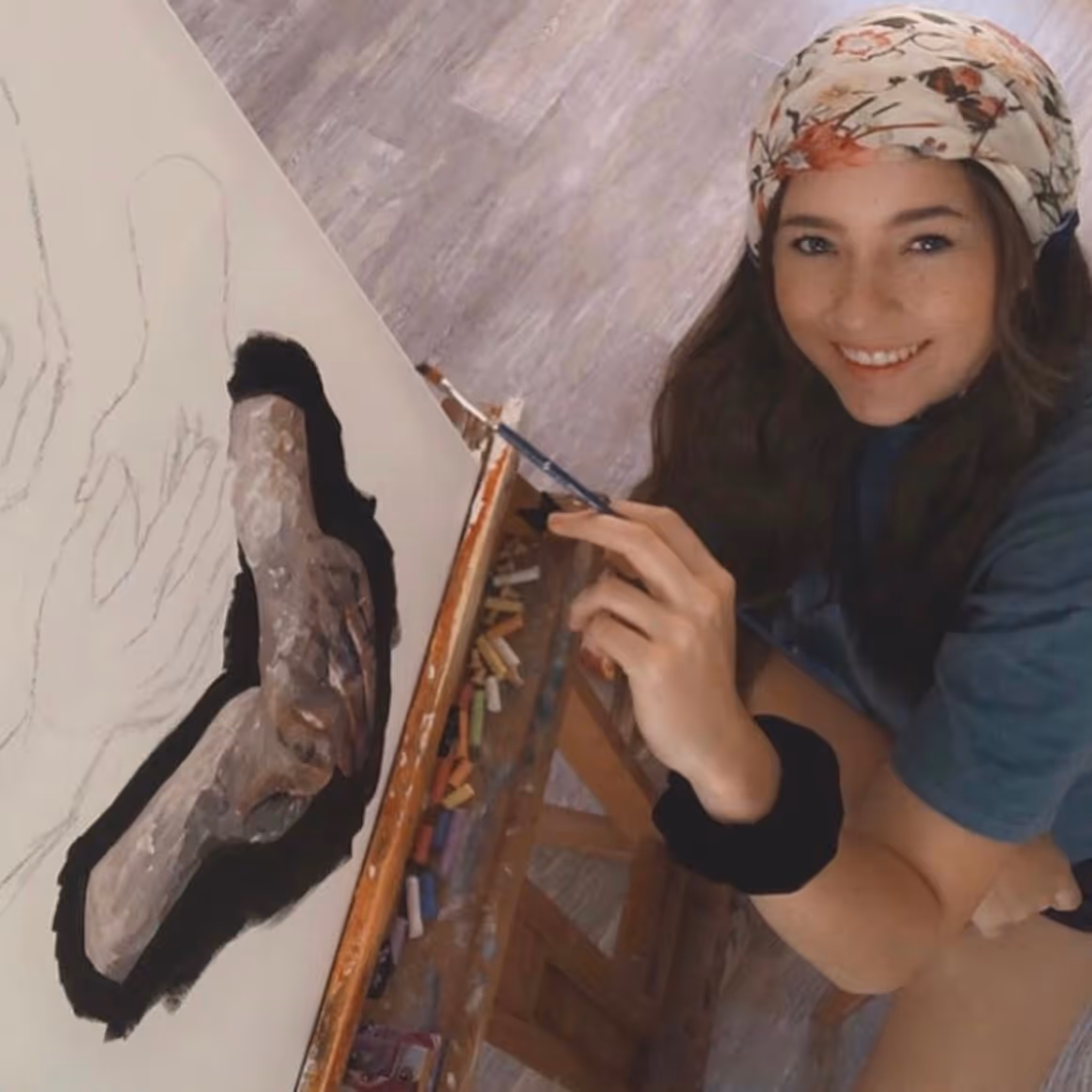 Travin, portfolio student, smiling while painting her large-scale piece of hands.