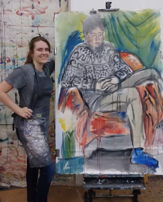 Lydia, Portfolio Program graduate, proudly showing off her large-scale painting of a clothed live model.