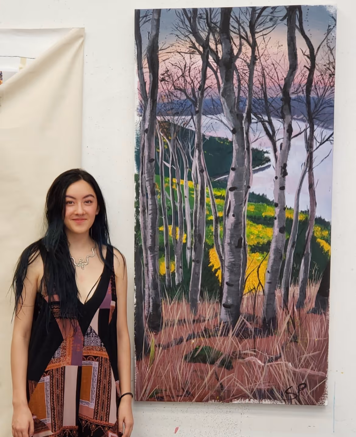 Sofia, Portfolio Program graduate, smiling and standing next to one of her first large-scale paintings. 