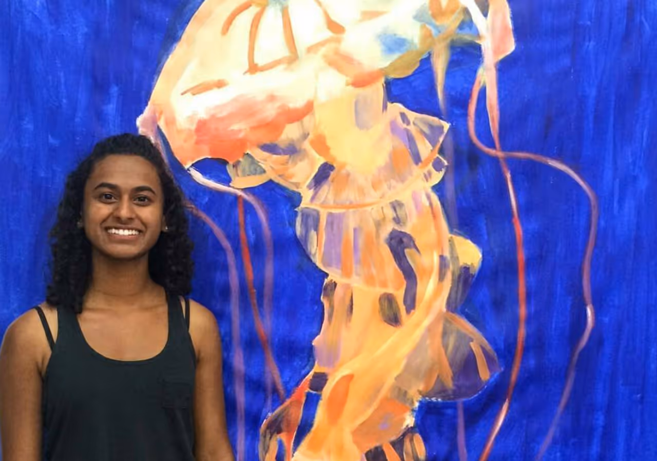 A high school student standing in front of her large scale painting of a jelly fish that she created in the College Art Portfolio Program.