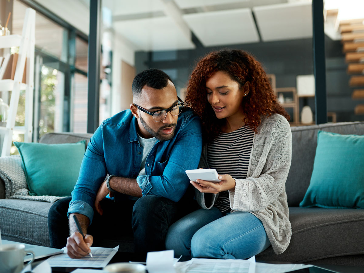 Couple sitting on a couch reviewing documents with a calculator and pen in a modern living room.