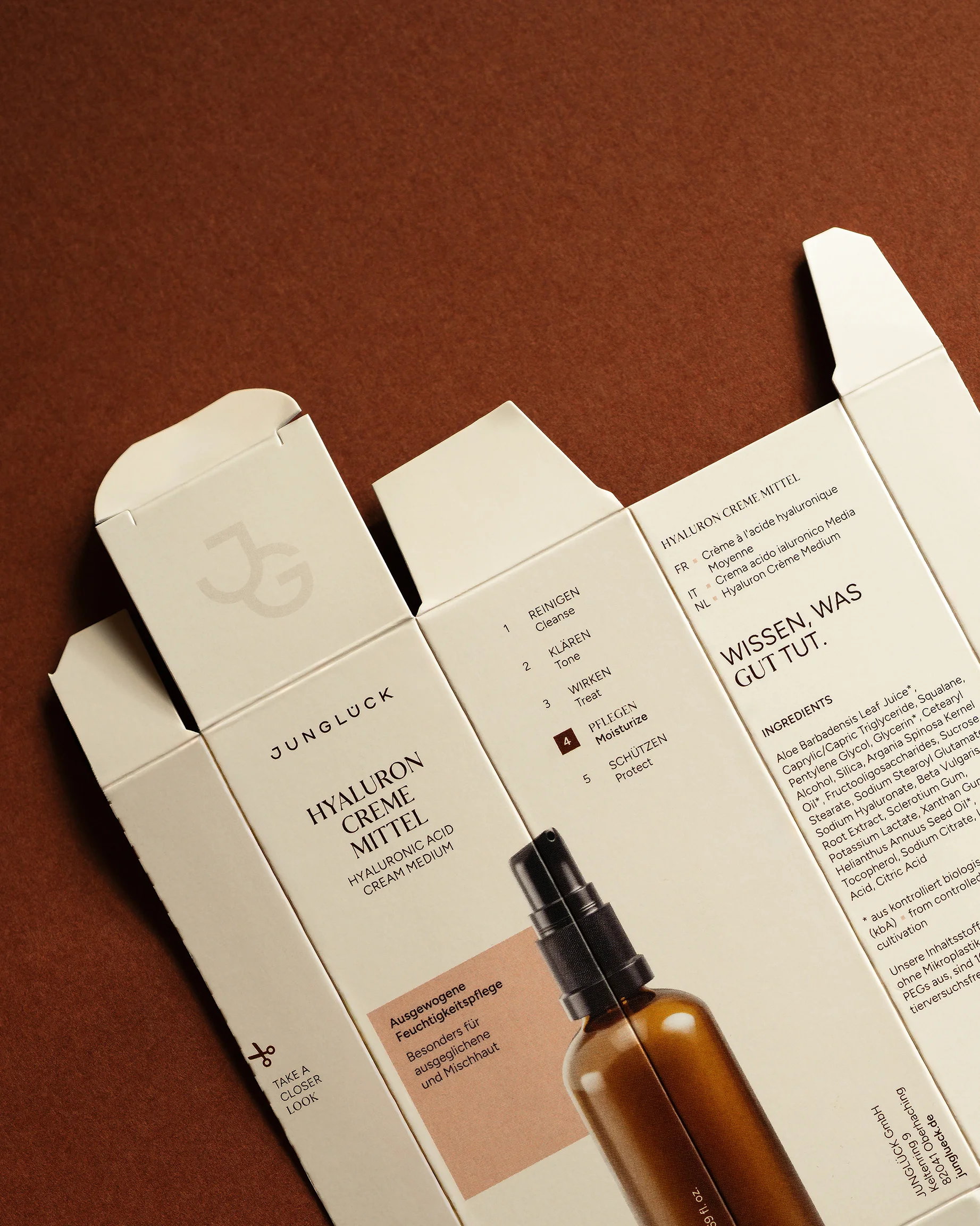 Opened packaging box for Junglück Hyaluron Creme Mittel showing product information and ingredients on a brown background.