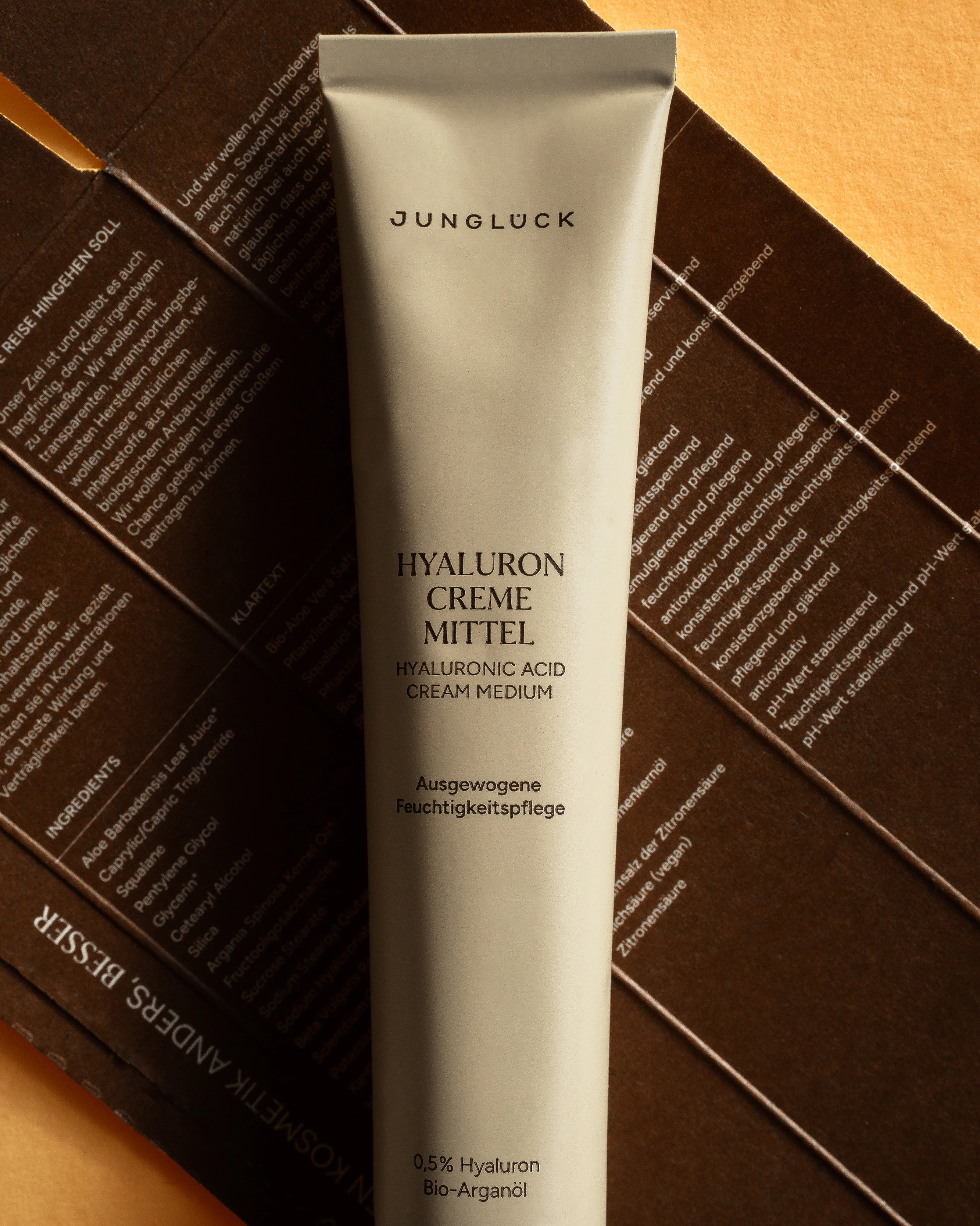 Tube of JUNGLÜCK Hyaluron Creme Mittel with extra cardboard packaging in background on light brown surface.