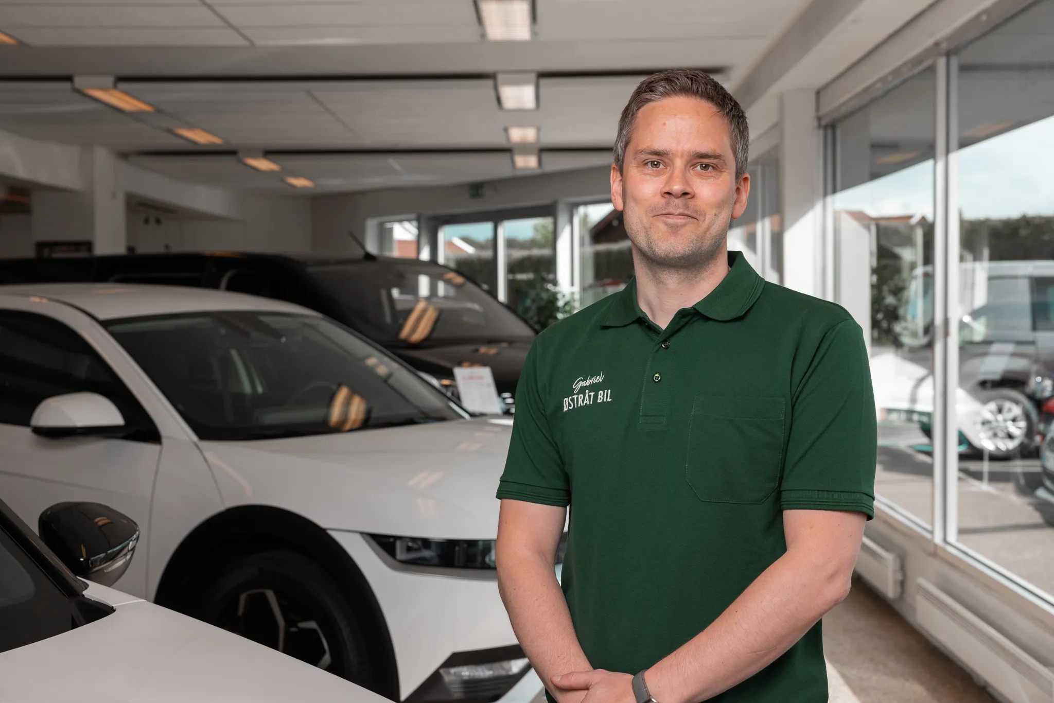Ansatt hos Østråt Bil står i bilforhandlerens showroom foran utstilte biler.