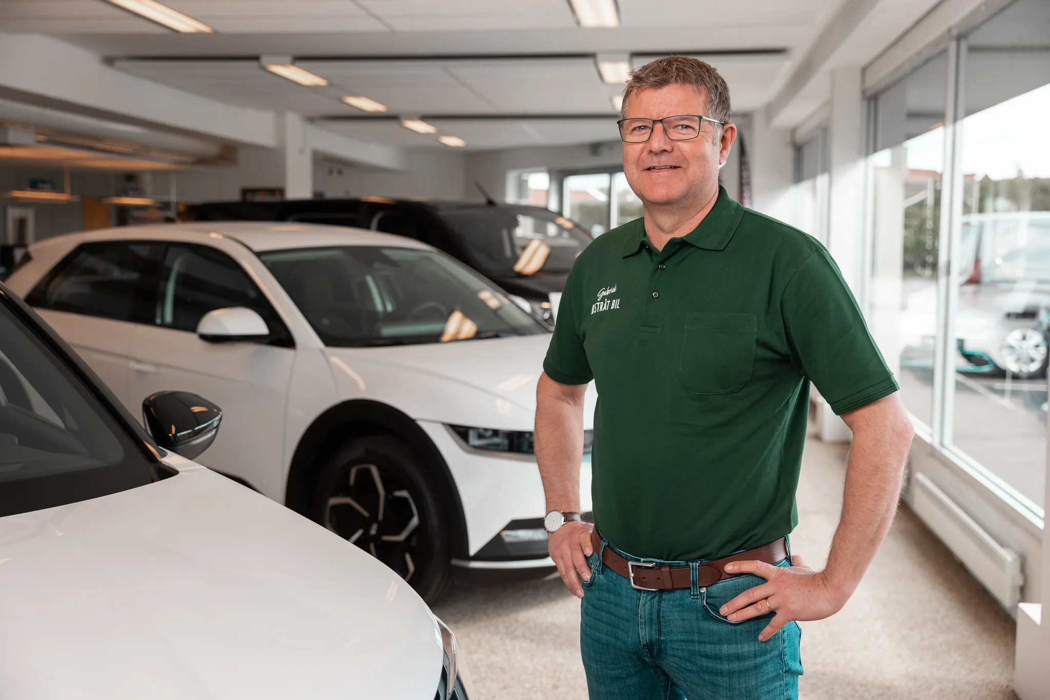 Ansatt hos Østråt Bil står i bilforhandlerens showroom omgitt av biler.