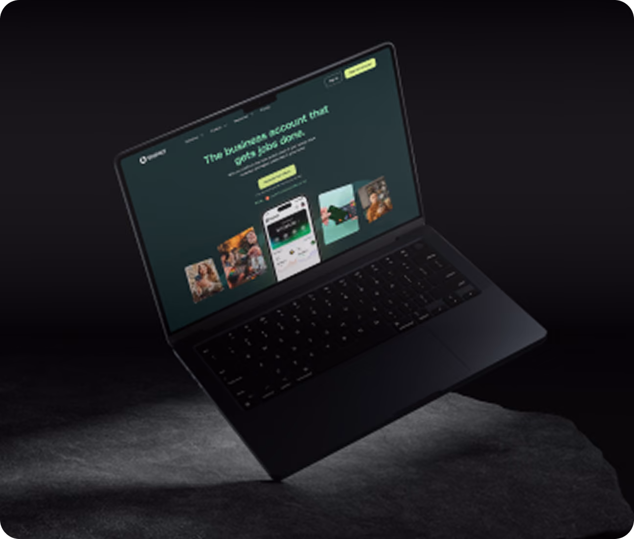 Black laptop floating above a dark textured surface with its screen displaying a green-themed business account webpage featuring images and app screenshots.