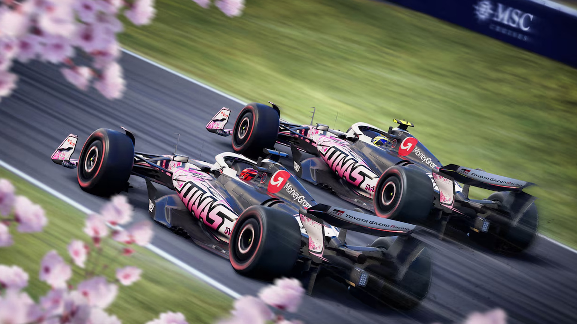 Two Haas cars racing fast on a track with cherry blossoms in the corner