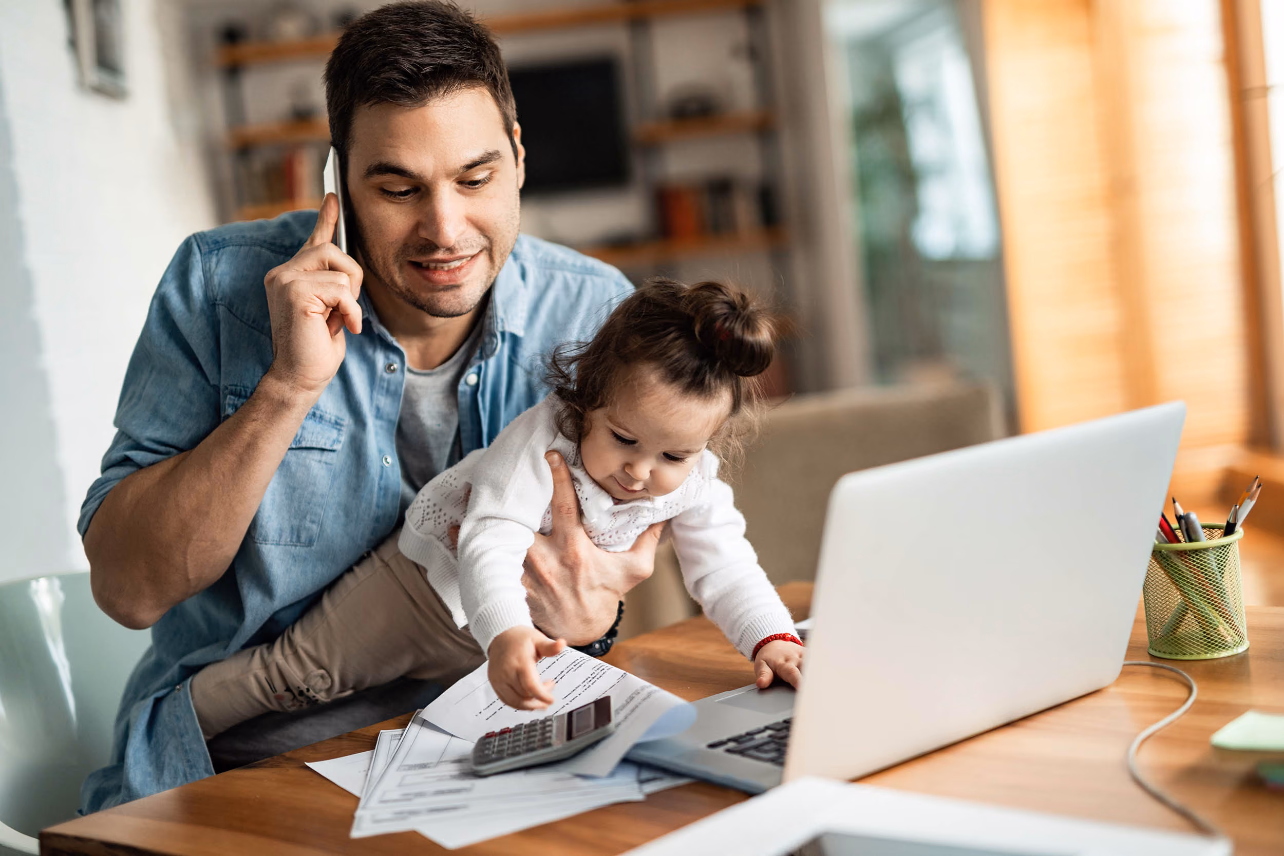 A father busy working from home while taking care of his toddler in arms