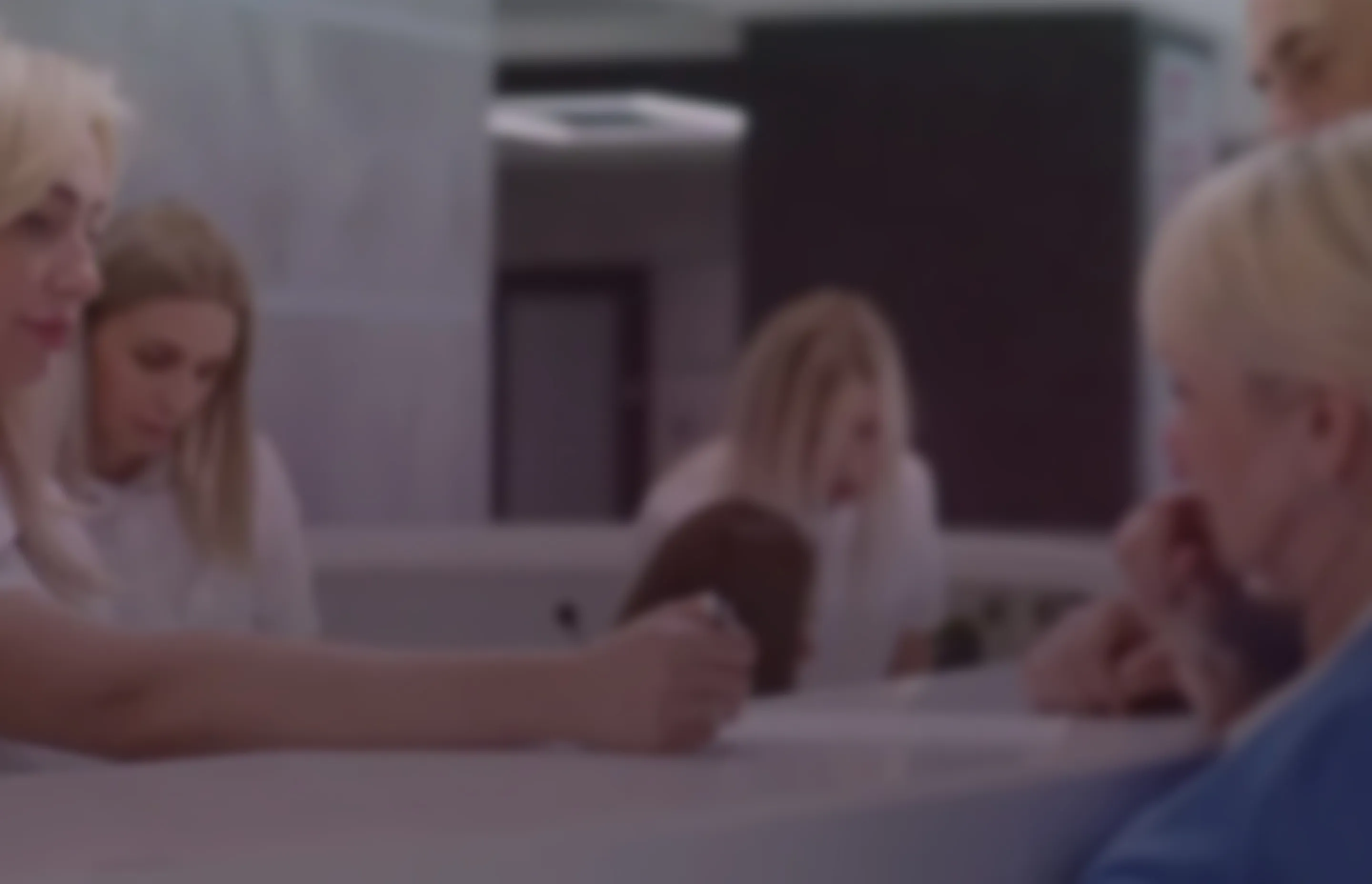 Blonde receptionist assisting elderly couple at a modern white counter in a brightly lit office or clinic.