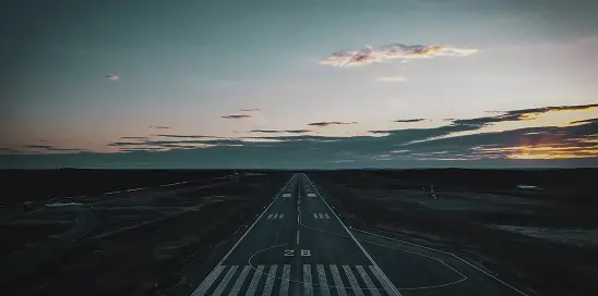 Airplane runway at dusk with a dark landscape and a cloudy sky with faint light on the horizon.