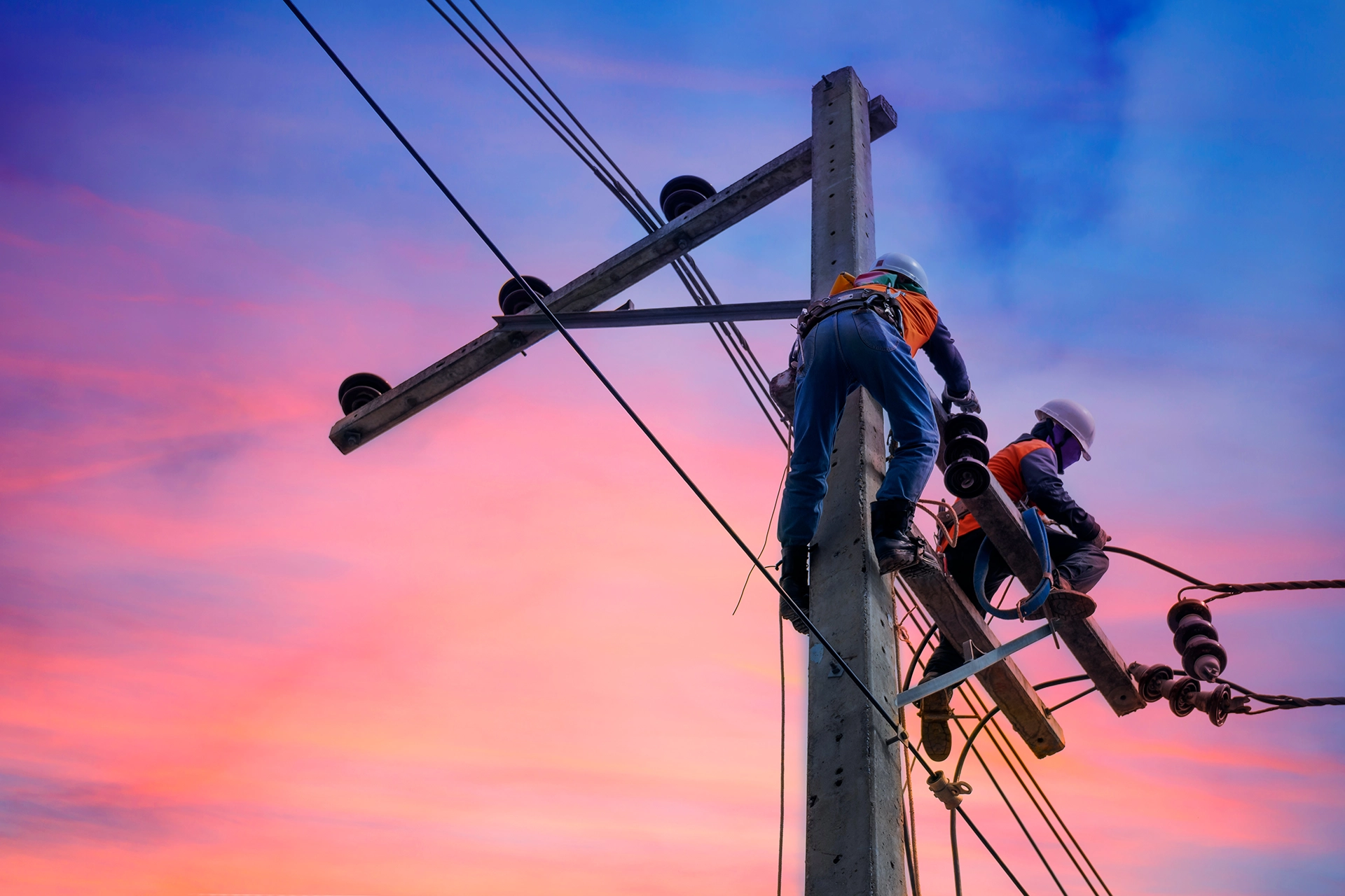 Two repairmen working with safety gear on an electrical pole