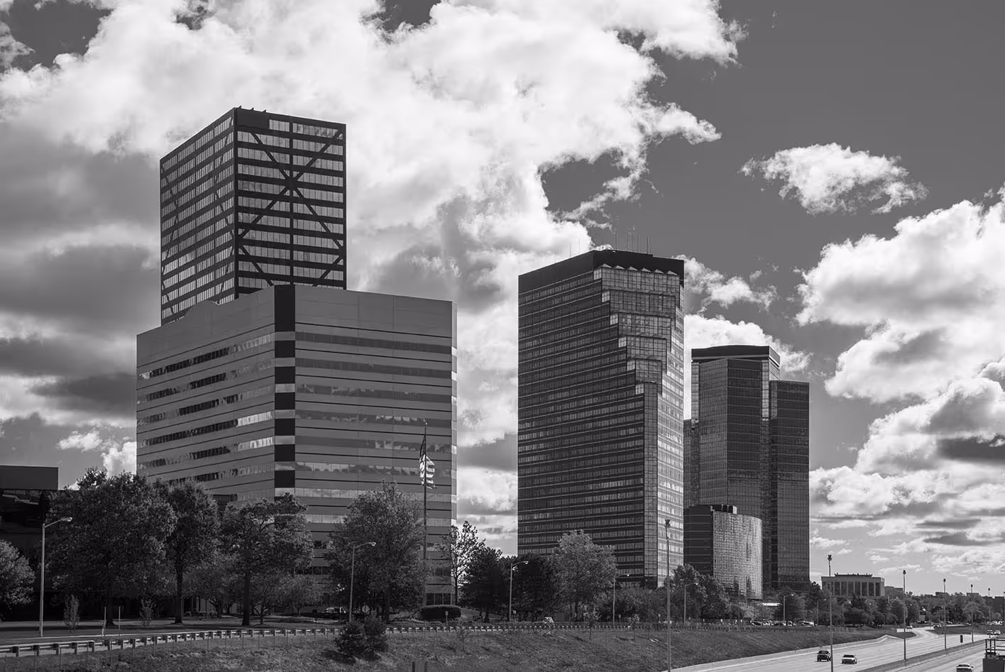 City skyline with modern office buildings along a highway under a partly cloudy sky.