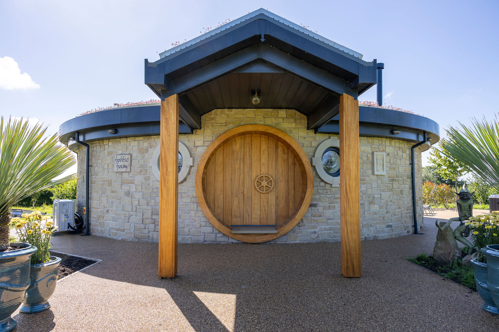 Stone round house with a large wooden circular door under a roofed porch supported by two wooden pillars.