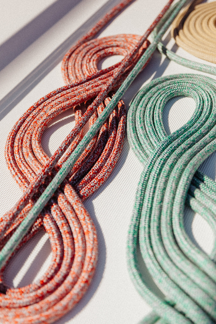 Coiled climbing ropes in orange, green, and tan lying on a textured white surface.
