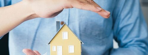 person protecting a wooden house by putting their hand over it
