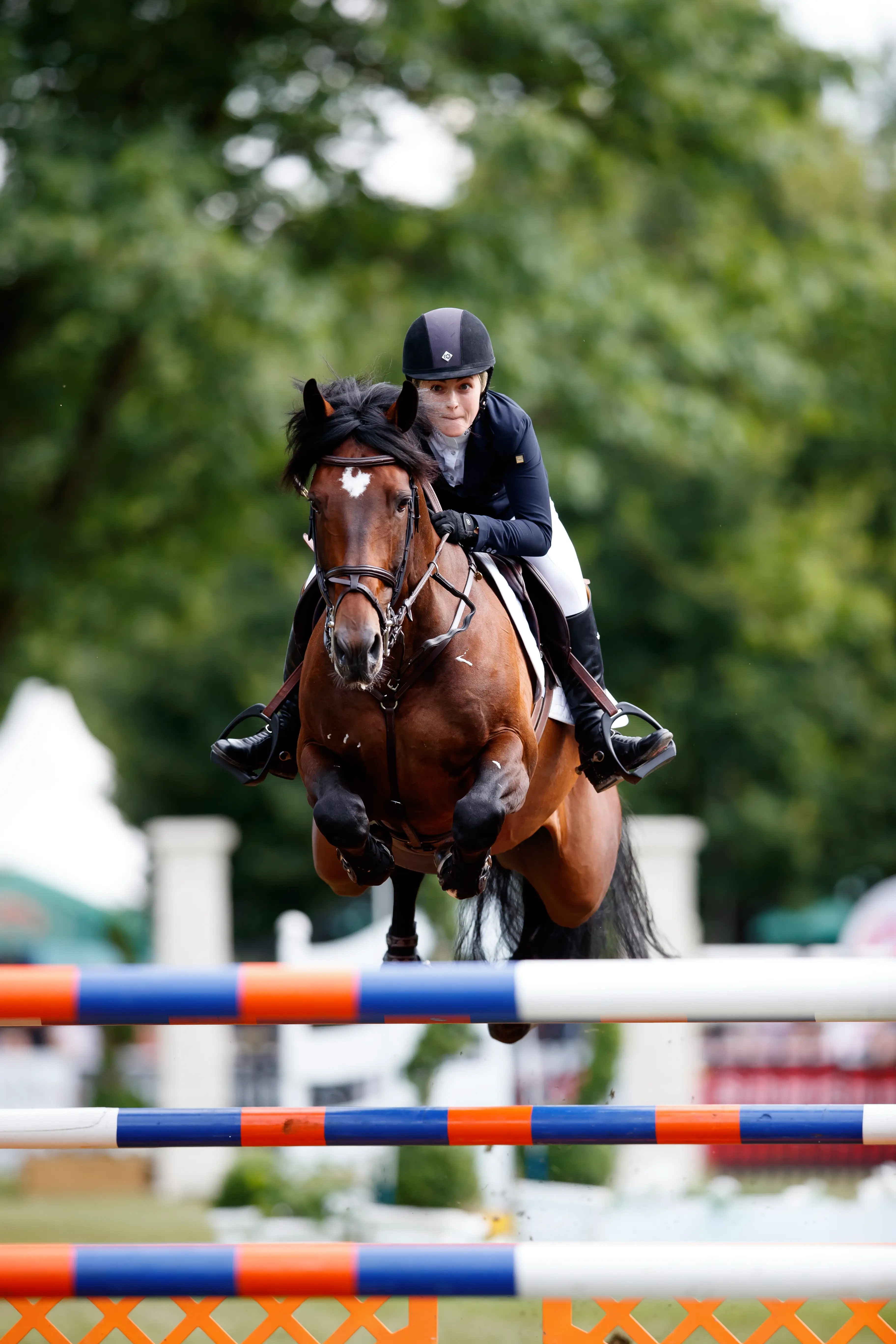 Chloe Reid riding her horse over a jump at an outdoor competition, poised and elegant in the saddle.