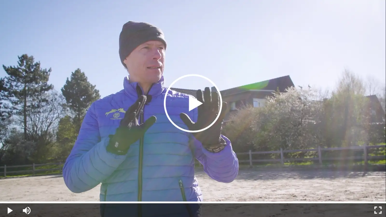 Christian Ahlmann im blauen Reitoutfit und Mütze bei einer Trainingseinheit im Freien, erklärt gestikulierend eine Übung.