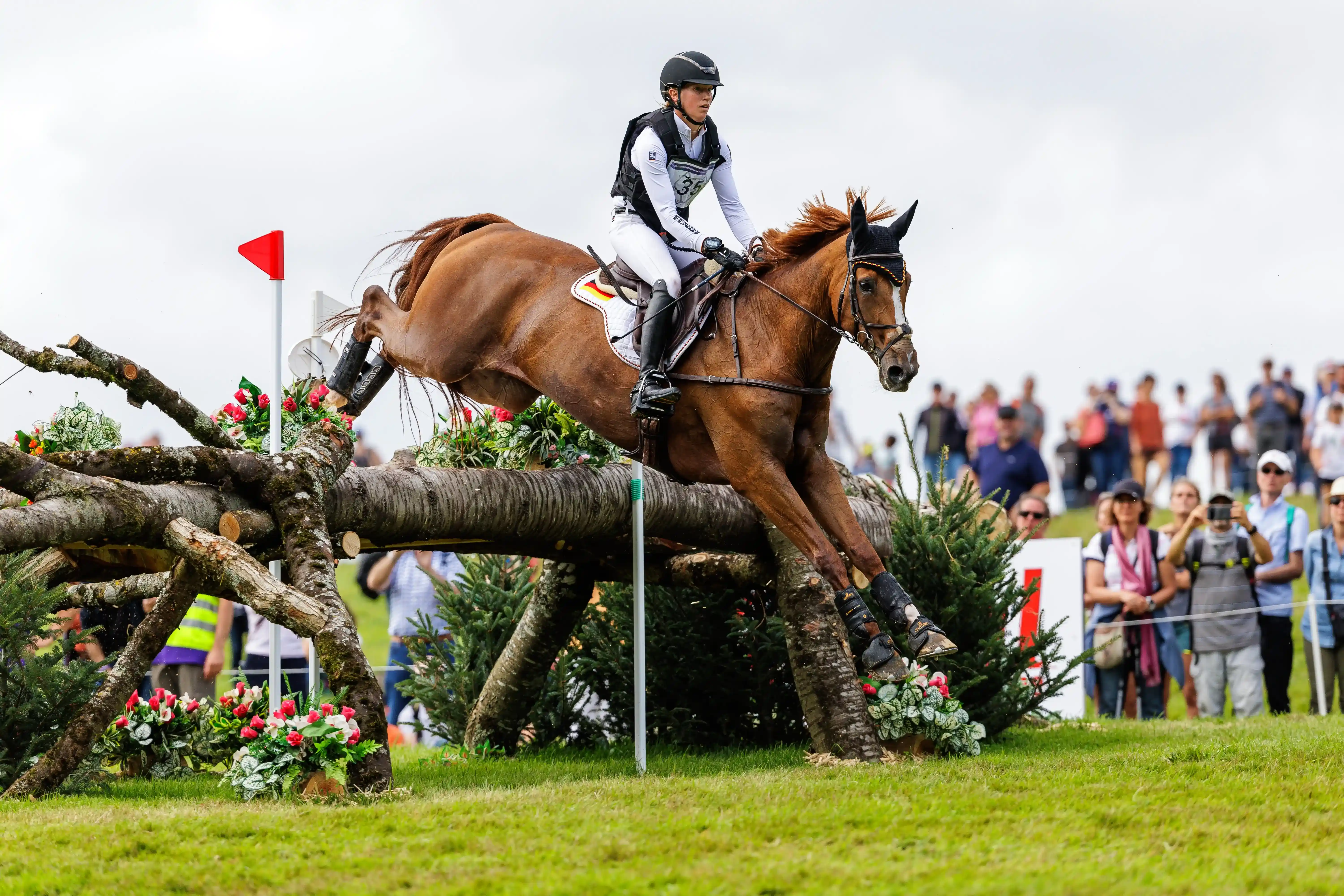 Sandra Auffarth beim Geländeritt im Vielseitigkeitsturnier, springt mit ihrem Pferd über ein Naturhindernis vor Zuschauern