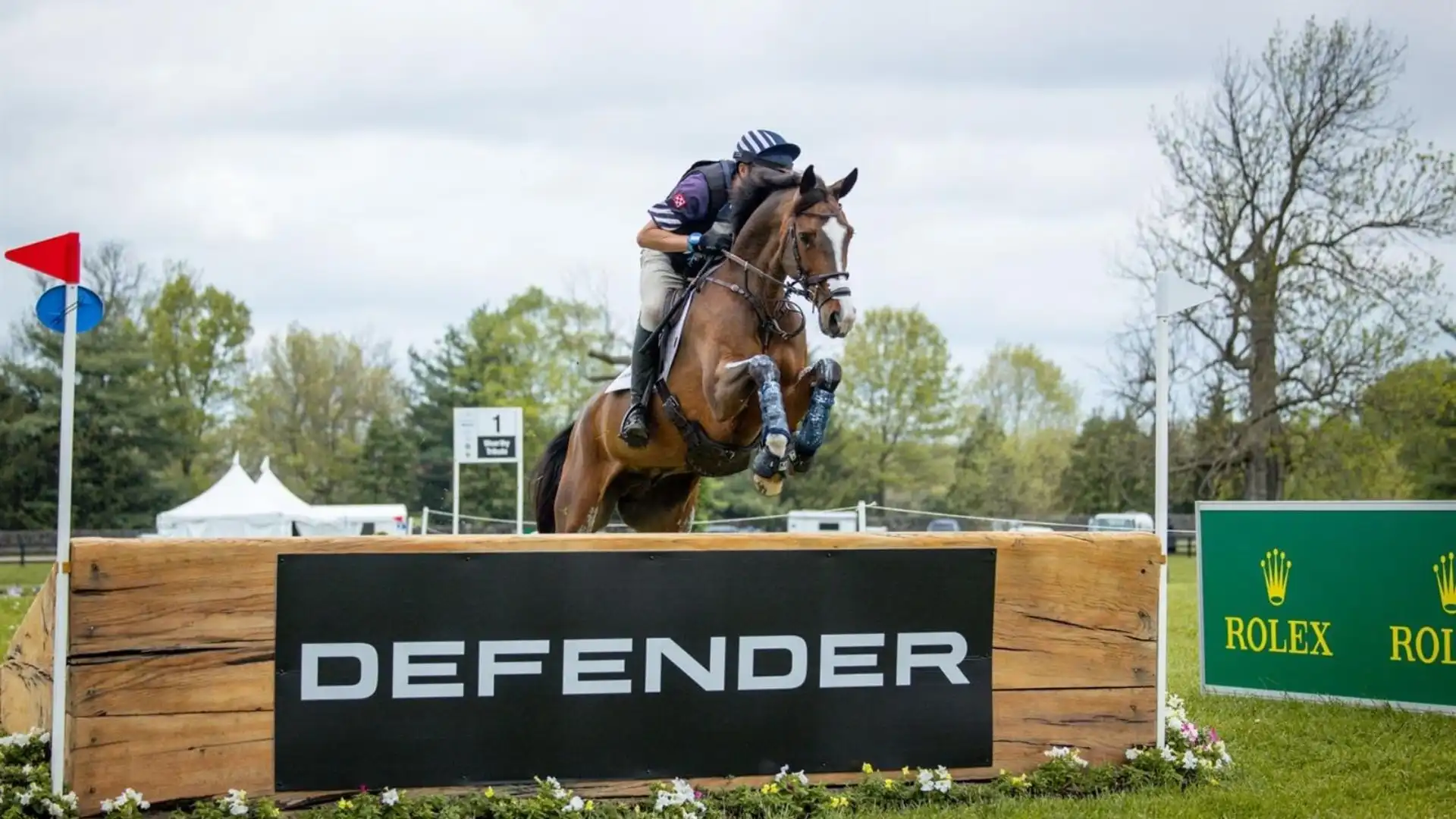 Ein Reiter auf einem braunen Pferd springt im Gelände über ein Defender-Hindernis beim Kentucky Three-Day Event.