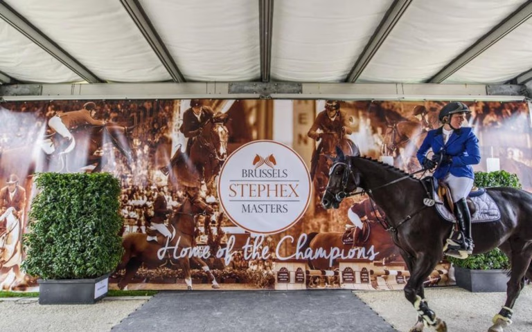 Springreiter auf dunklem Pferd vor einer großen Brussels Stephex Masters-Wand mit dem Schriftzug „Home of the Champions“.