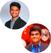 Two young men smiling, one in a dark suit with a gray shirt against a light background, and the other in a suit with a blue shirt and tie at an event with red and white balloons.