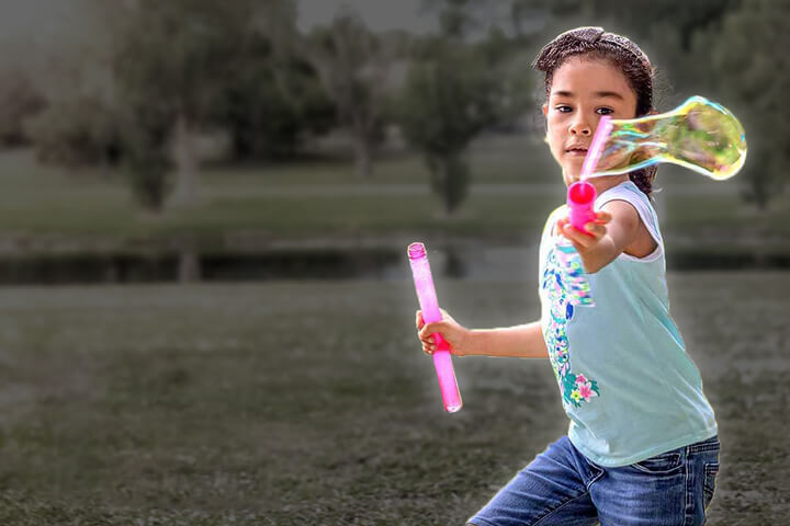 Girl running through field with bubble wand and bubbles