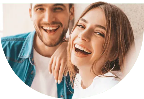 Ein Mann und eine Frau lachen fröhlich in die Kamera und zeigen ihr strahlendes Lächeln.