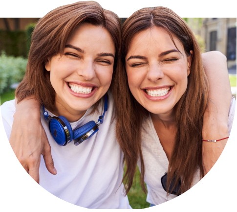 Zwei junge Frauen lächeln glücklich in die Kamera und umarmen sich