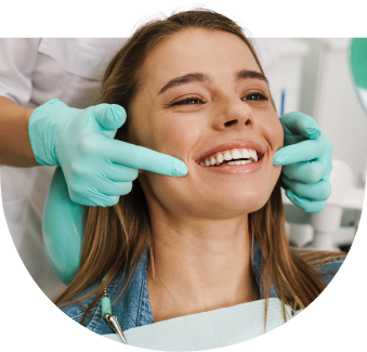 Junge Frau sitzt lachend im Behandlungsstuhl beim Zahnarzt, während eine Person mit Handschuhen ihre Zähne kontrolliert – Symbolbild für Zahngesundheit und Vertrauen in die Behandlung