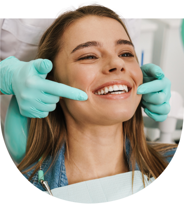 Junge Frau sitzt lachend im Behandlungsstuhl beim Zahnarzt, während eine Person mit Handschuhen ihre Zähne kontrolliert – Symbolbild für Zahngesundheit und Vertrauen in die Behandlung