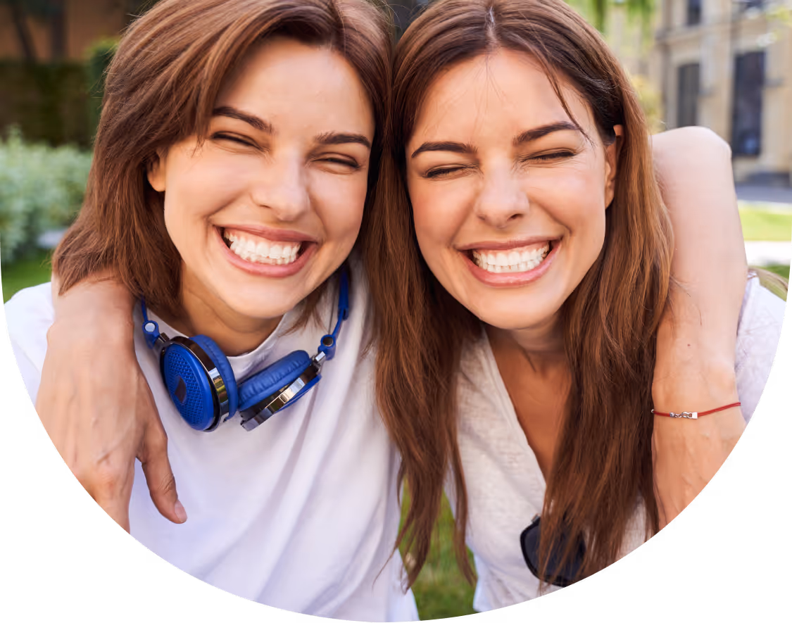 Zwei junge Frauen lächeln glücklich in die Kamera und umarmen sich