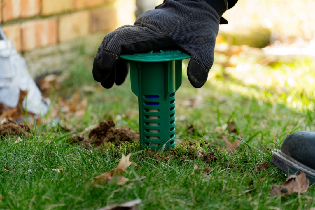 Technician installing a termite bait station in the ground near a home