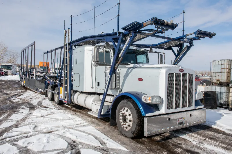 Car hauler truck with empty upper and lower decks parked on a snowy lot for heavy-duty transport service.