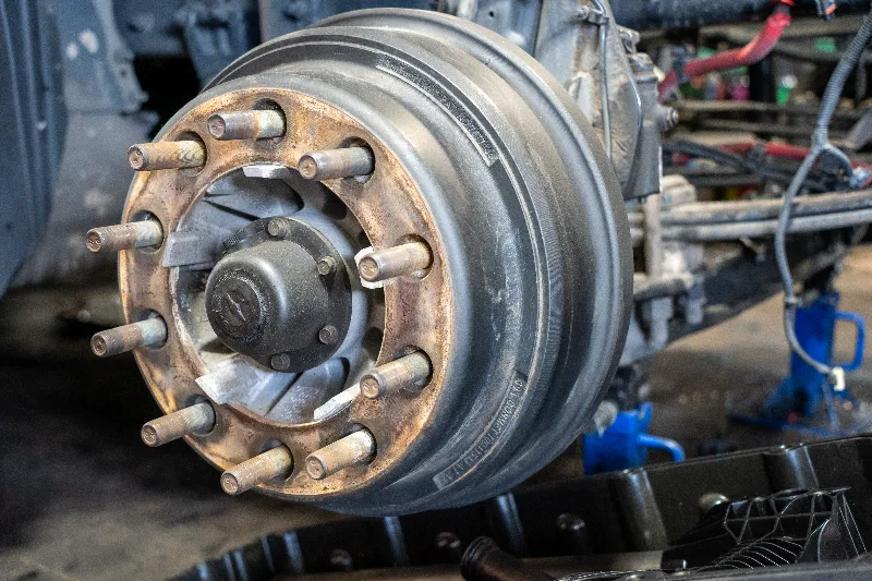 Brake repair close-up of heavy-duty truck hub and brake drum with wheel studs in shop bay.