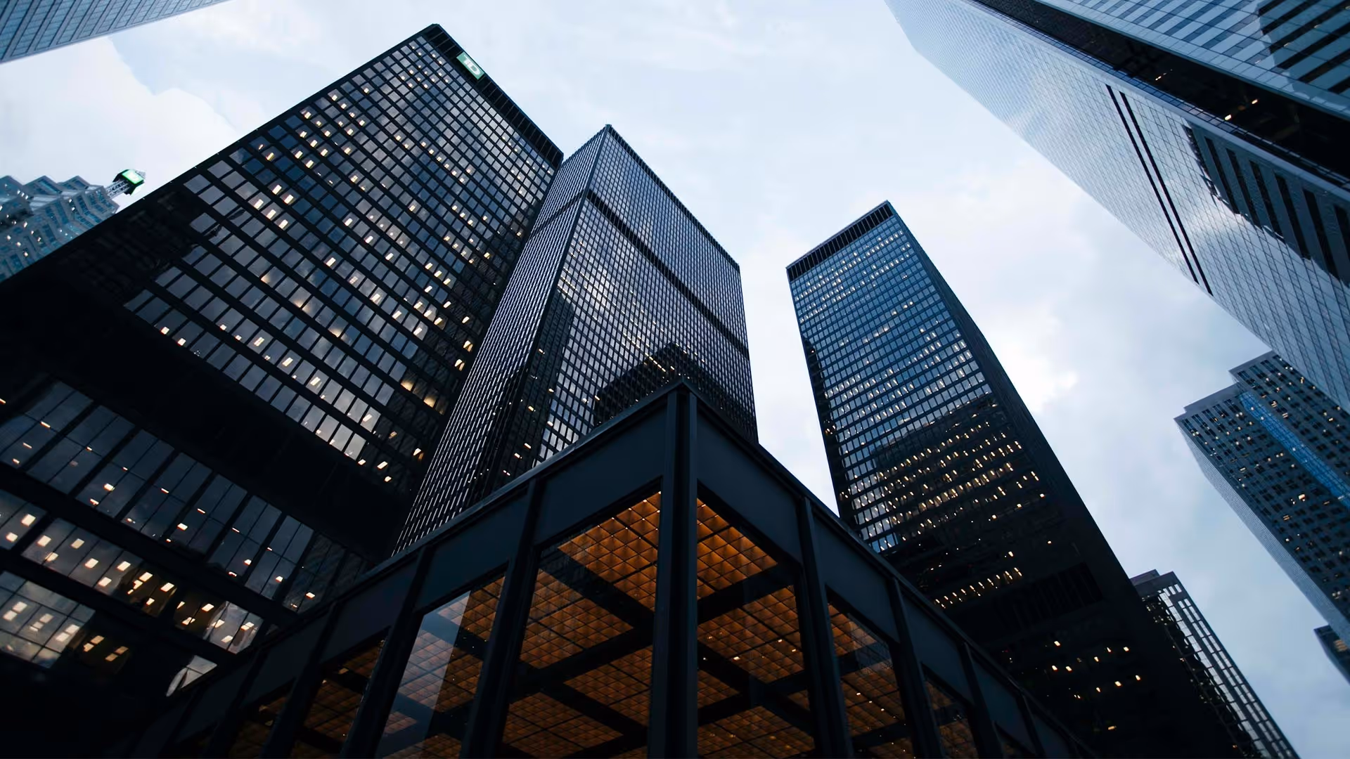 Low-angle view of modern glass skyscrapers against a cloudy sky in a cityscape.