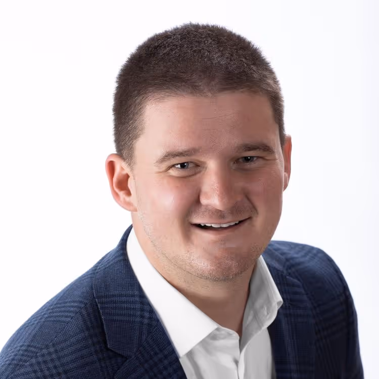 Smiling man with short dark hair wearing a blue checkered blazer and white shirt against a white background.