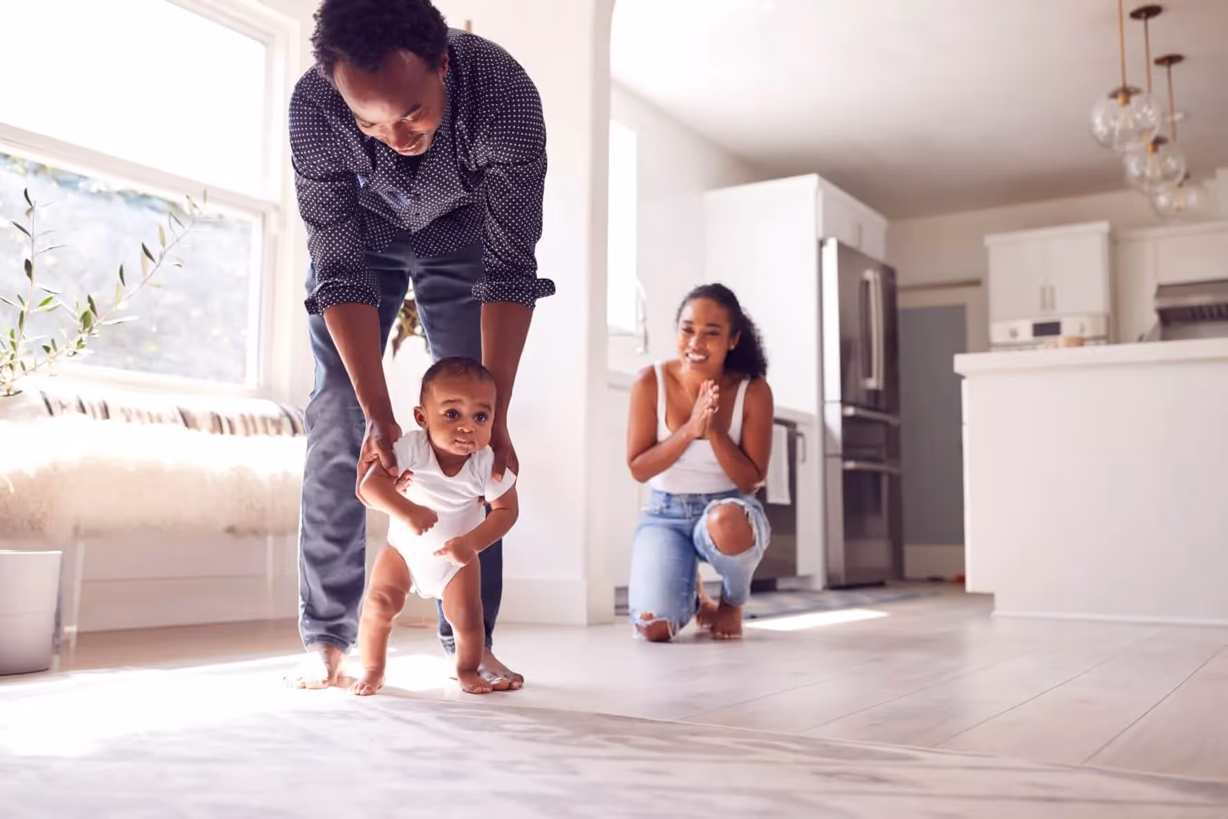A father walking his baby while mom claps and cheers behind them 
