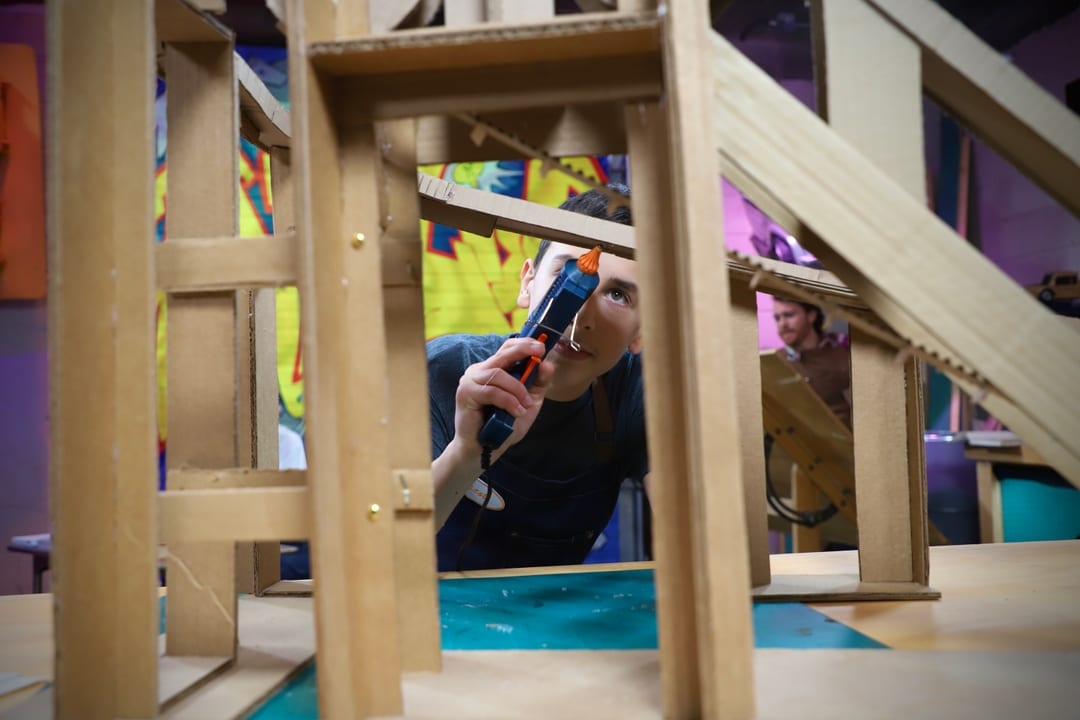 Un garcon colle une structure de carton avec un pistolet a colle