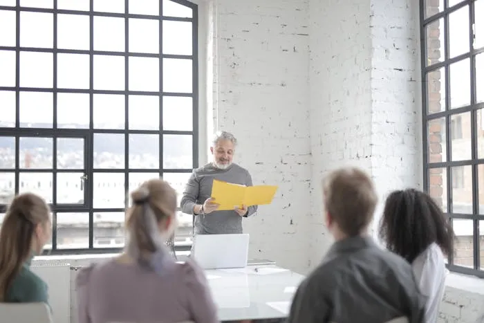 Man presenting to a group in a modern office with large windows.