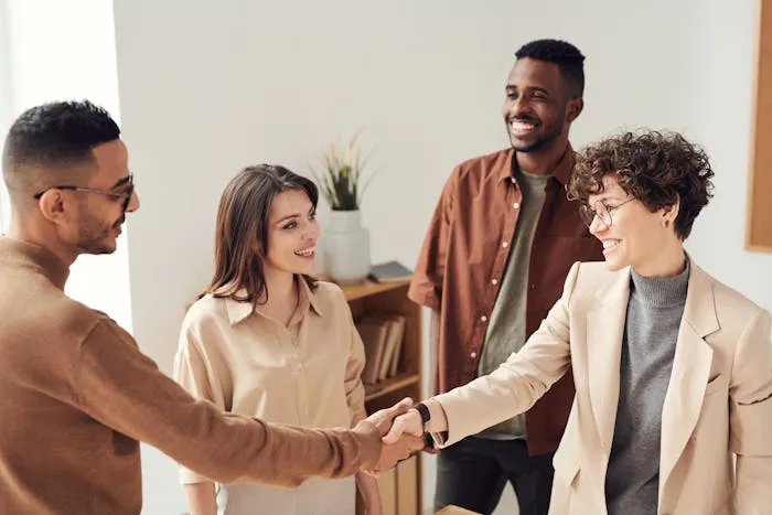 Four people in casual business attire shaking hands in an office environment.
